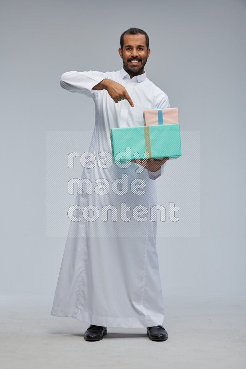 Saudi man Wearing thob standing holding gift box on Gray background