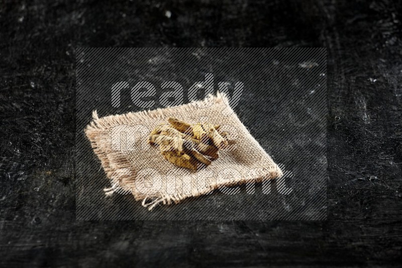 Dried turmeric whole fingers on a burlap piece of fabric on textured black flooring