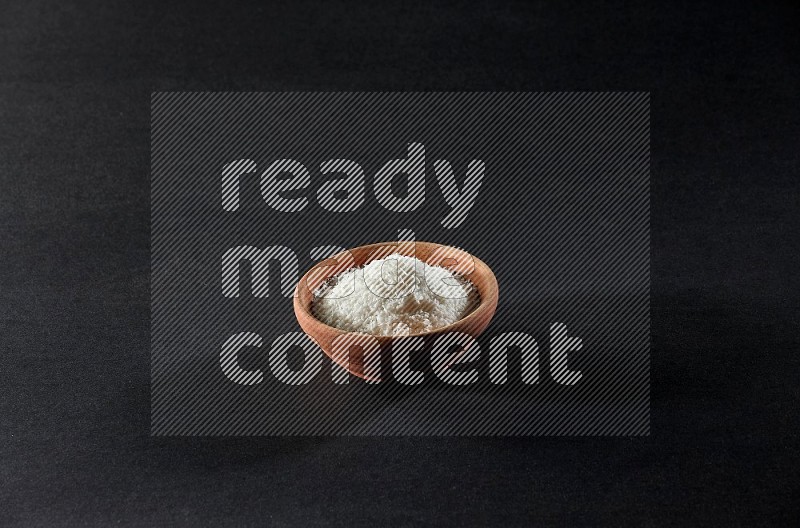 A wooden bowl full of desiccated coconut on a black background in different angles
