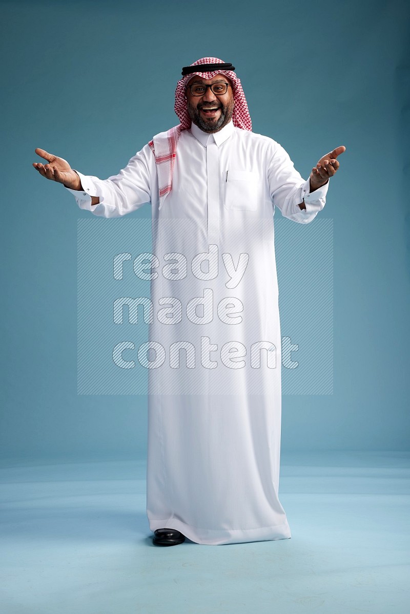 Saudi Man with shimag Standing Interacting with the camera on blue background