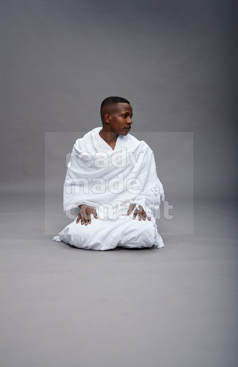 A man wearing Ehram sitting on floor praying on gray background
