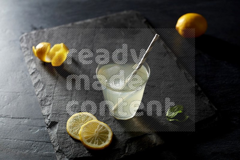 A glass of lemon juice with a straw on black background
