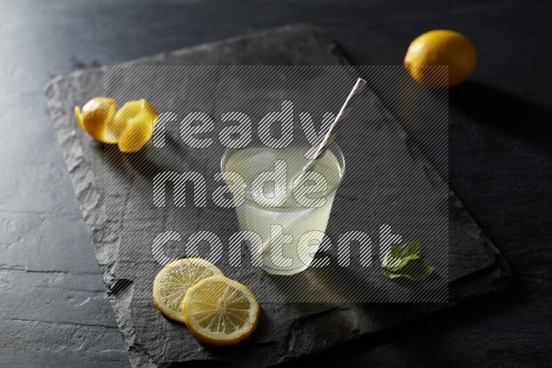 A glass of lemon juice with a straw on black background