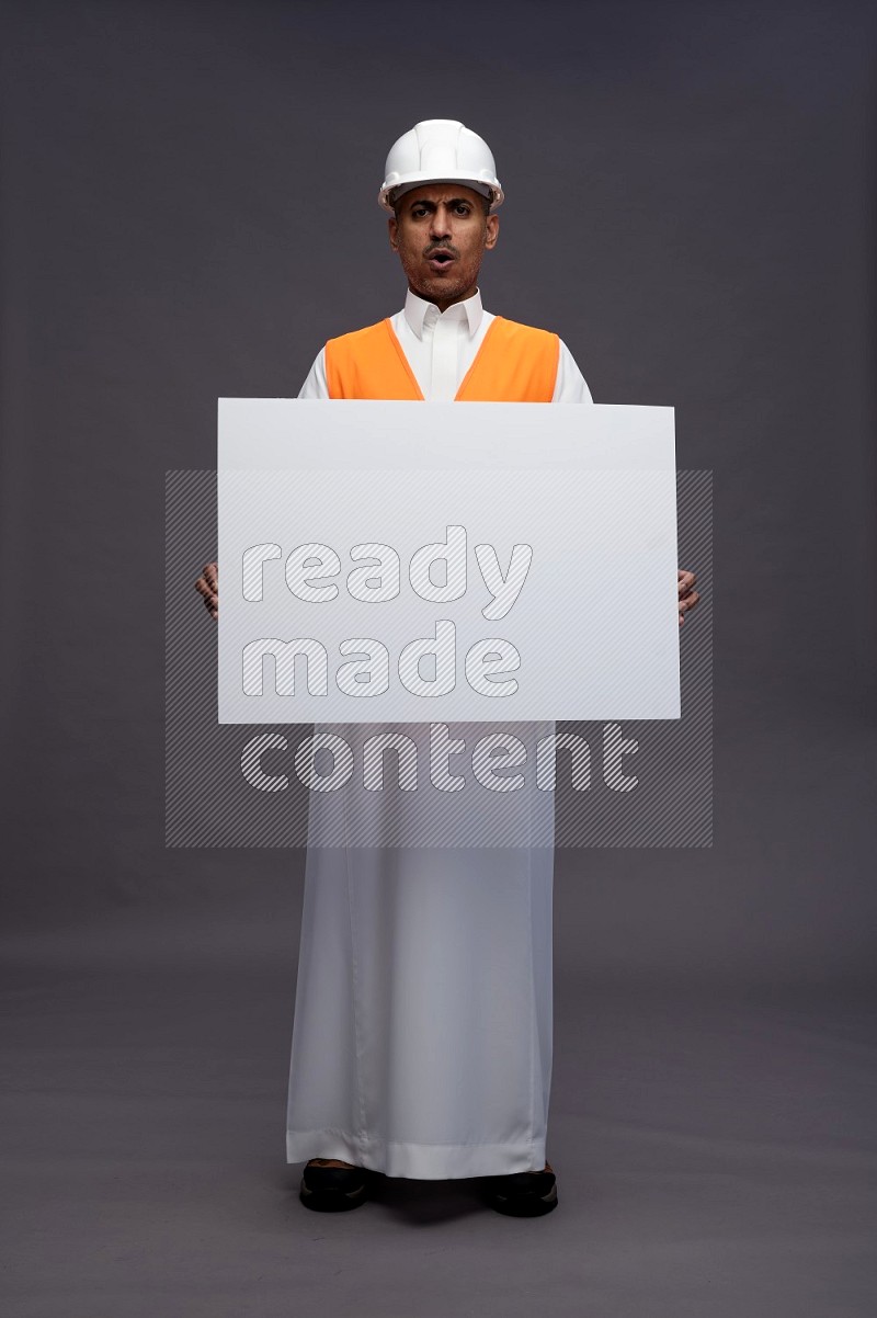 Saudi man wearing thob with engineer vest standing holding board on gray background