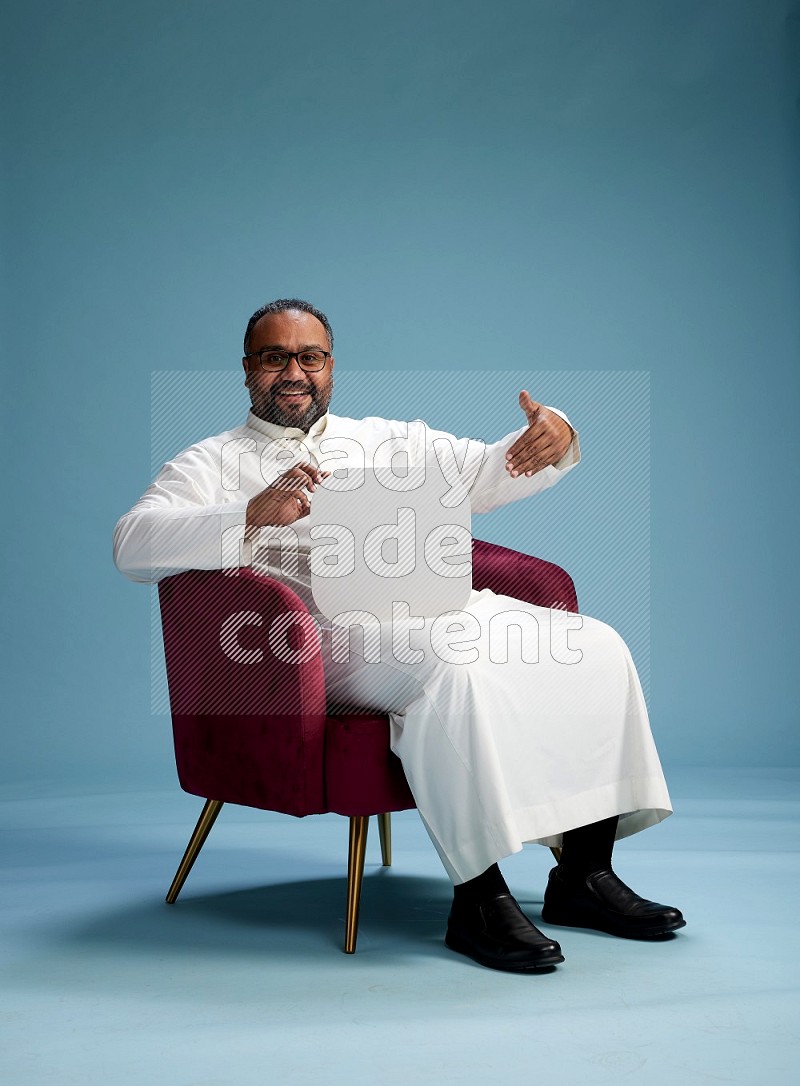 Saudi Man without shimag sitting on chair holding social media sign on blue background