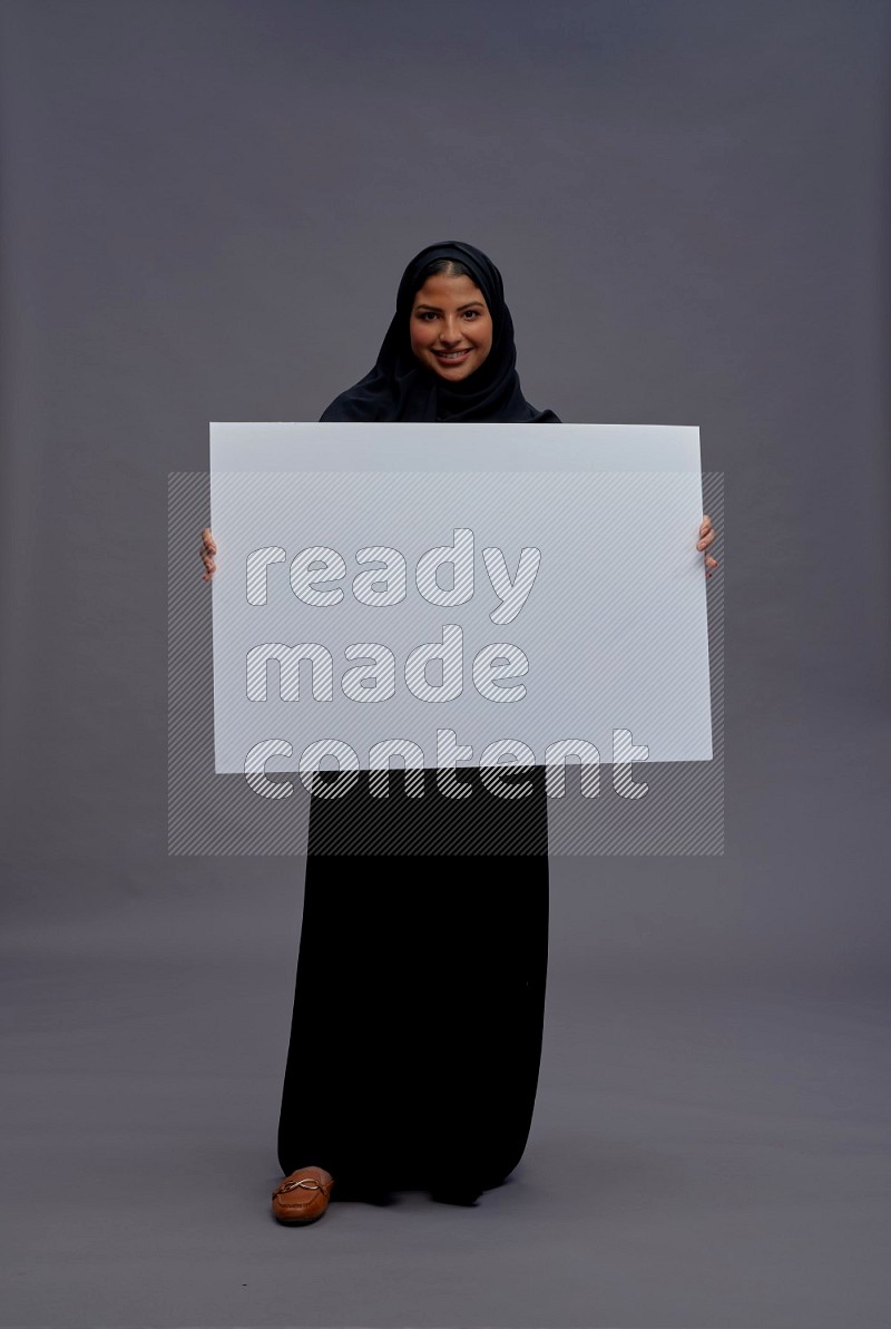 Saudi woman wearing Abaya standing holding white board on gray background