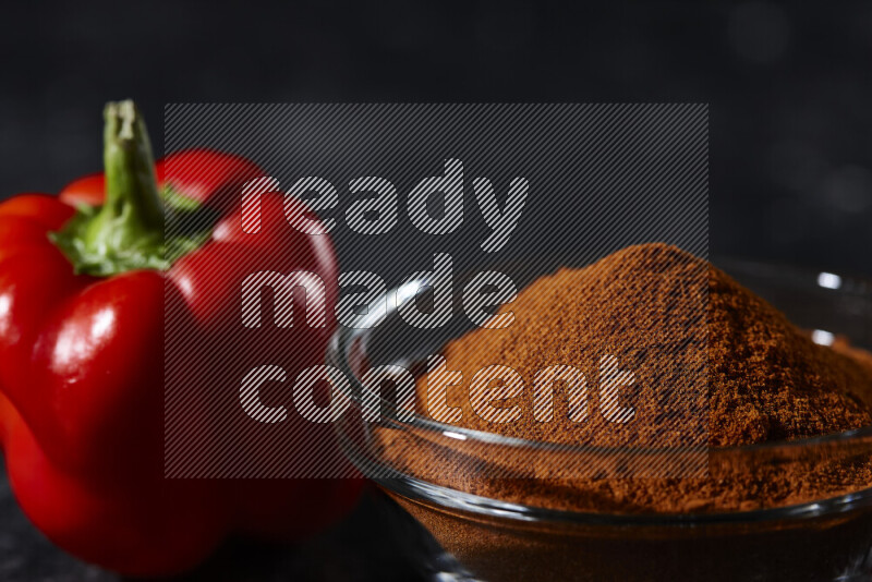 A glass bowl full of ground paprika powder on black background