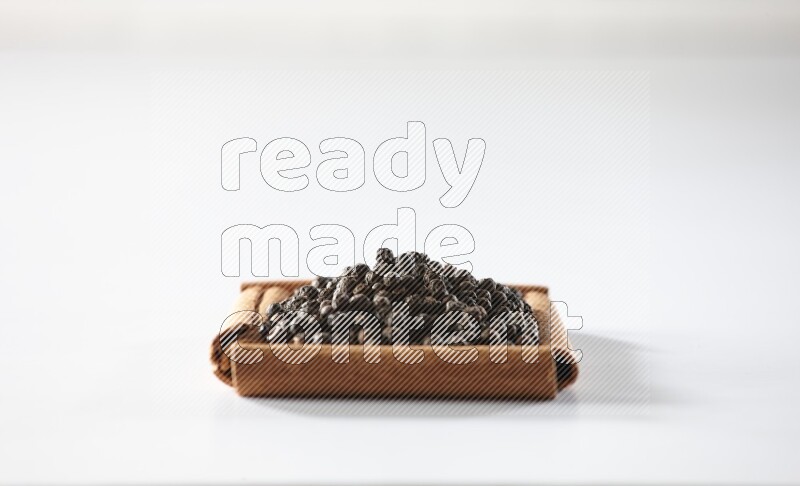 A single square of cinnamon sticks full of black pepper on white flooring