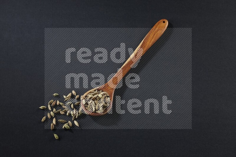 A wooden ladle full of cardamom on black flooring