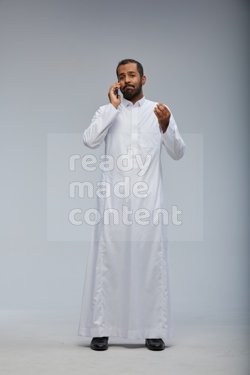 Saudi man wearing Thob standing talking on phone on Gray background