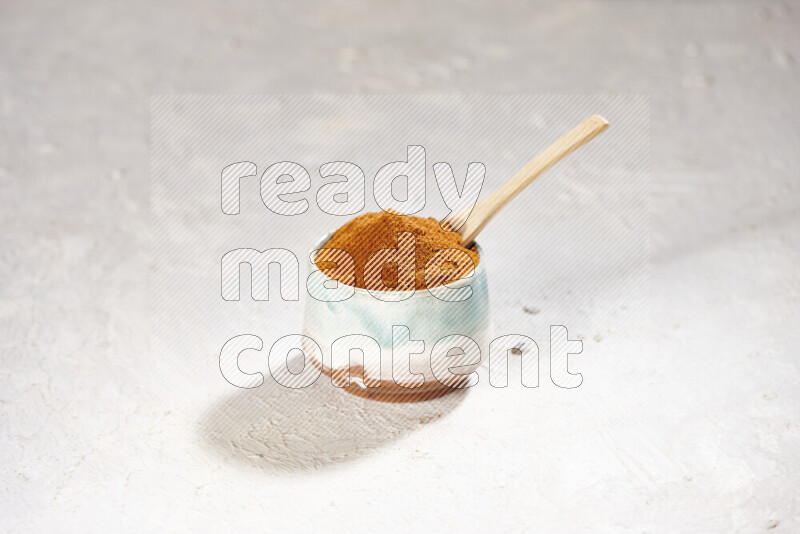 A colored pottery bowl full of ground paprika powder on white background