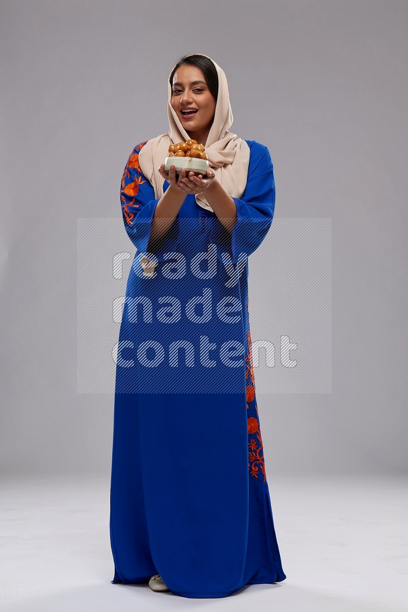 A Saudi woman standing wearing Jalabeya holding a plate of luqaimat