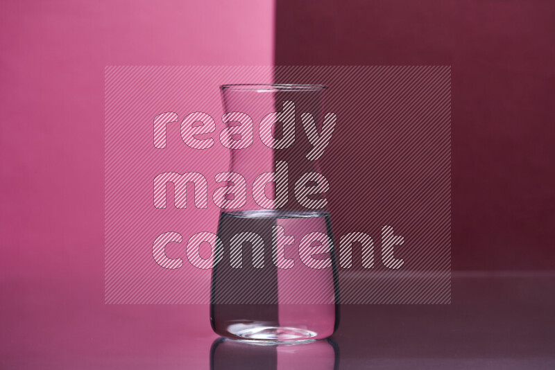 The image features a clear glassware filled with water, set against pink and dark red background