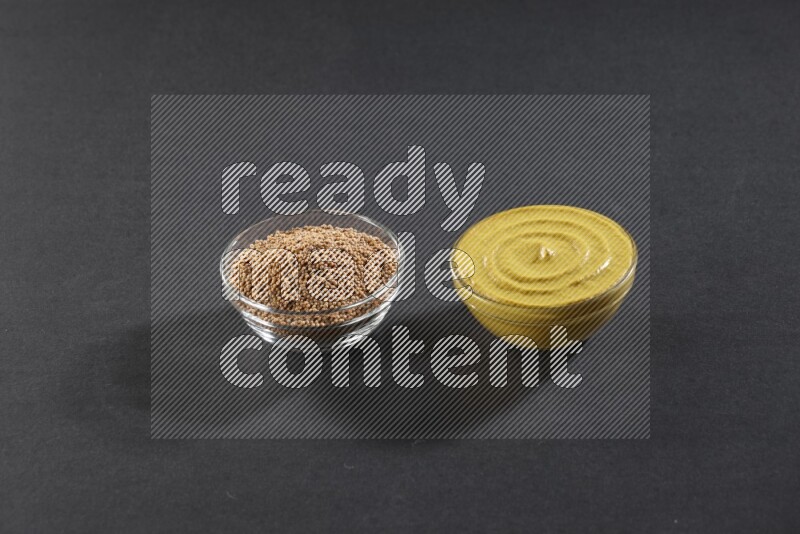 2 glass bowls, one full of mustard seeds and the other full of mustard paste on black flooring