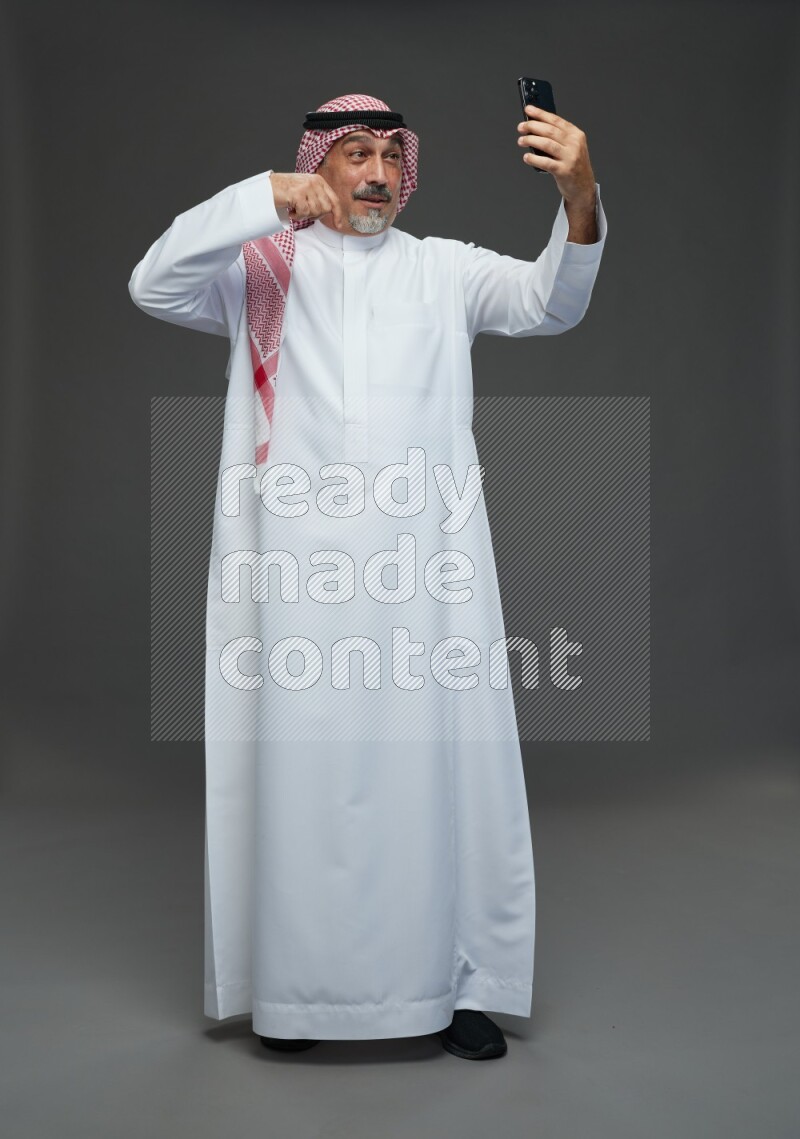Saudi man with shomag Standing taking selfie on gray background