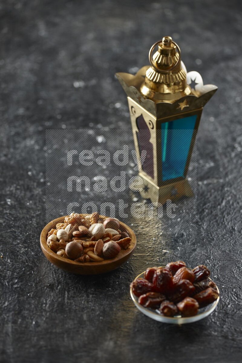 A golden lantern with different drinks, dates, nuts, prayer beads and quran on textured black background