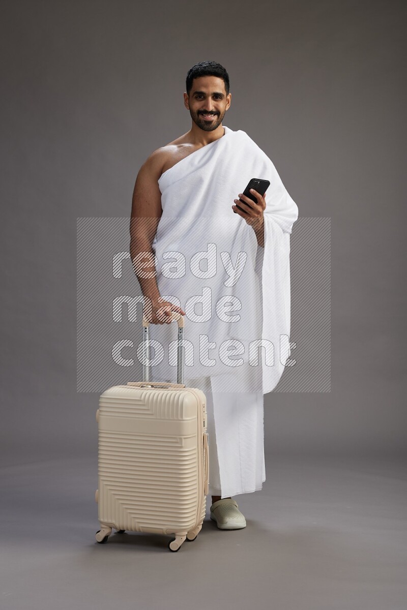 A man wearing Ehram Standing holding traveling bag on gray background