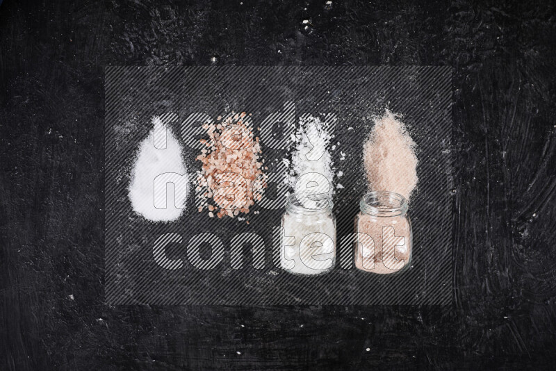 4 glass jars filled with table salt, coarse sea salt, fine himalayan salt and coarse himalayan salt on black background