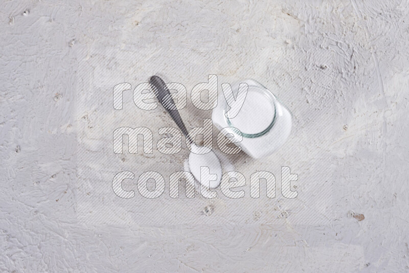 A glass jar full of fine table salt on white background