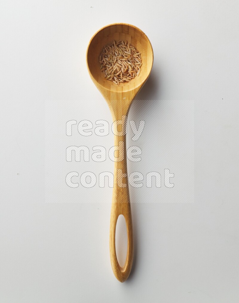 Top-view of a long grain brown rice inside a wooden spoon on white background