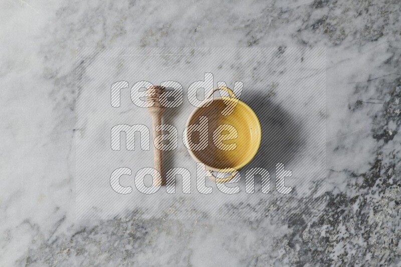 Multicolored pottery bowl with wooden honey dipper on the side on grey marble background
