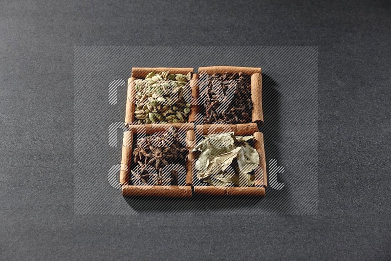 4 squares of cinnamon sticks full of star anise, cardamom, cloves and bay laurel leaves on black flooring