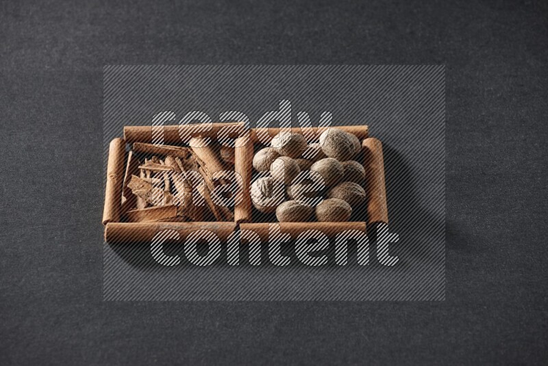 مربعان من أعواد القرفة ممتلئان بقطع من القرفة وجوزة الطيب علي خلفية سوداء