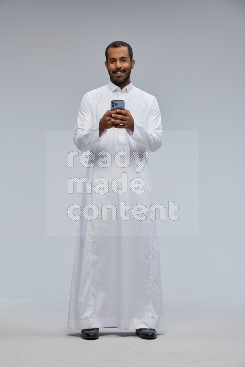 Saudi man wearing Thob standing texting on phone on Gray background