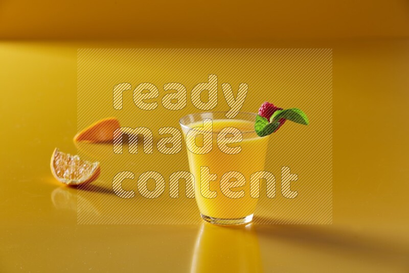 glass of orange juice with berry & mint on yellow background