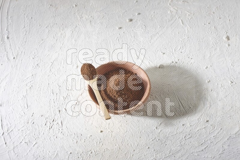 A wooden bowl and a wooden spoon full of cloves powder on a textured white flooring