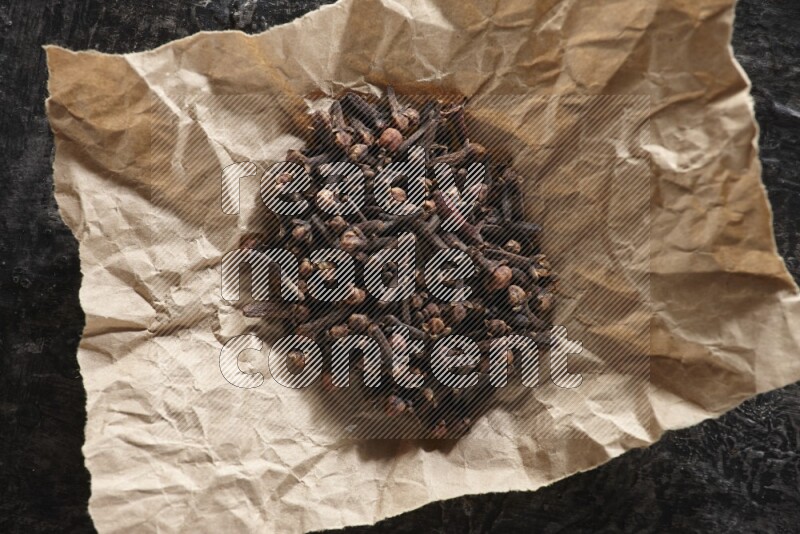 Cloves in crumpled piece of paper on a textured black flooring