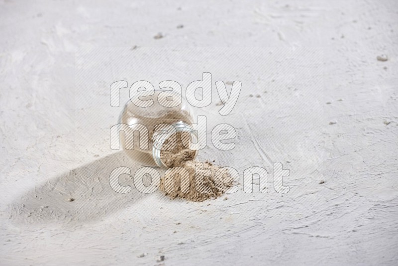 A glass spice jar full of garlic powder flipped and the powder came out on a textured white flooring in different angles
