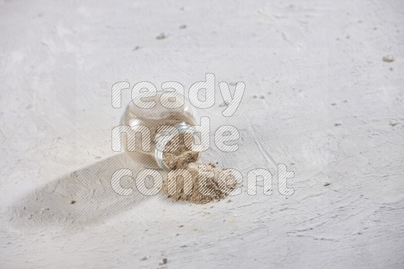 A glass spice jar full of garlic powder flipped over with the powder came out on a textured white flooring