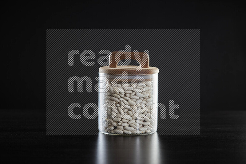 White beans in a glass jar on black background
