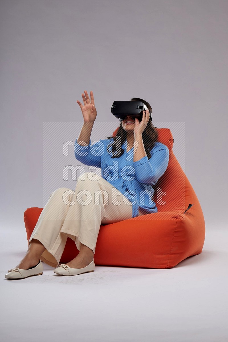 A woman sitting on an orange beanbag and gaming with VR