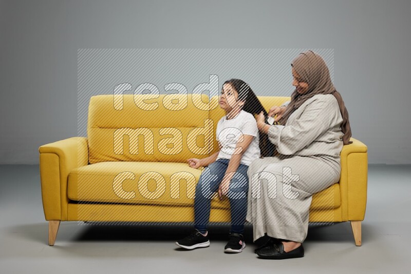 A mother sitting styling hair for her daughter on gray background