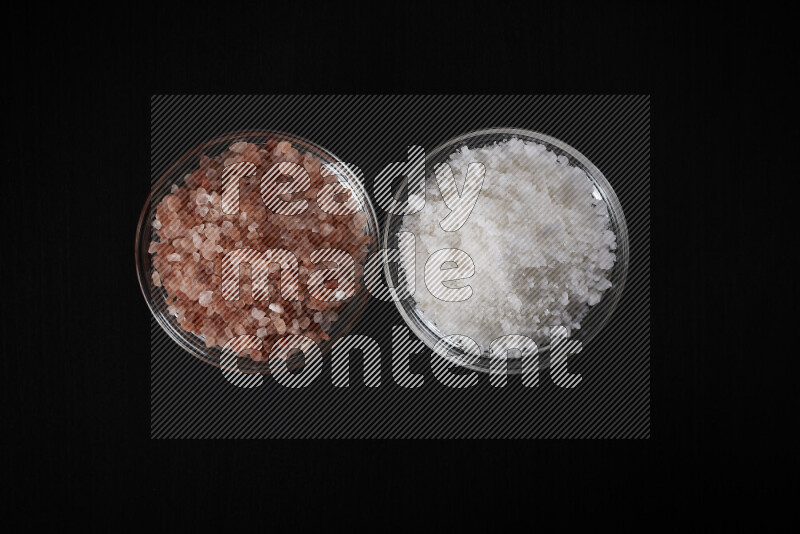 2 glass bowls one is filled with himalayan salt and the other with white salt on black background