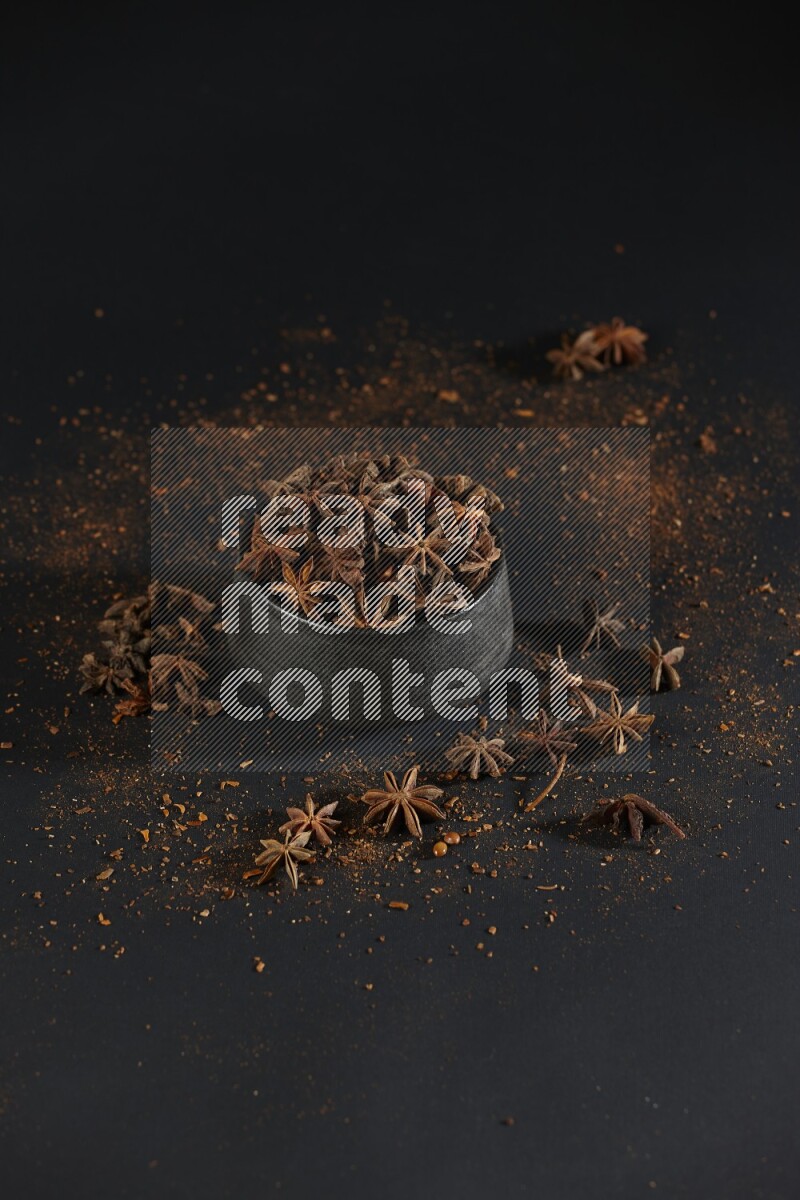 Star Anise in a black bowl with sprinkled anise on black flooring