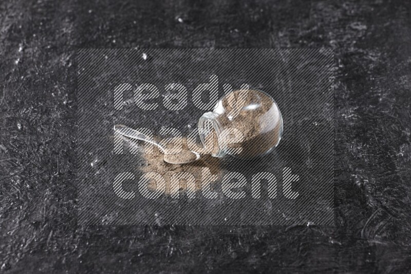 بودرة الفلفل الأسود في وعاء زجاجي مقلوب مع ملعقة معدنية مليئة بالبودرة علي خلفية سوداء