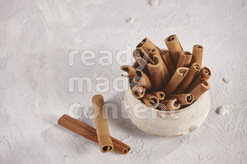 Cinnamon sticks in a beige bowl and more sticks beside it on white background