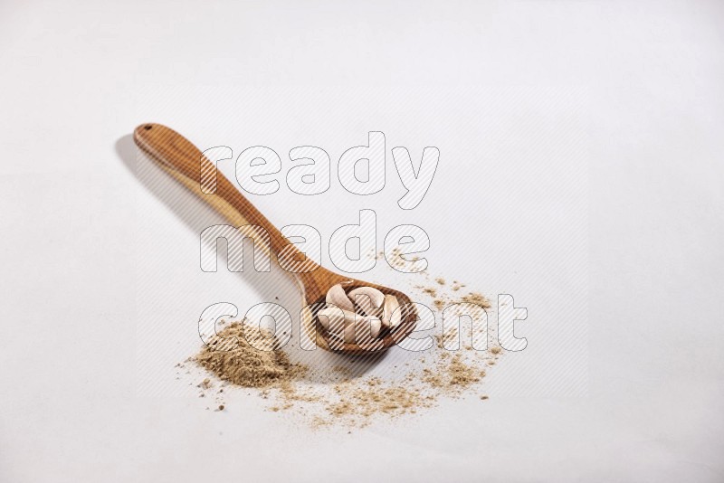 A wooden ladle full of garlic cloves on a white flooring in different angles