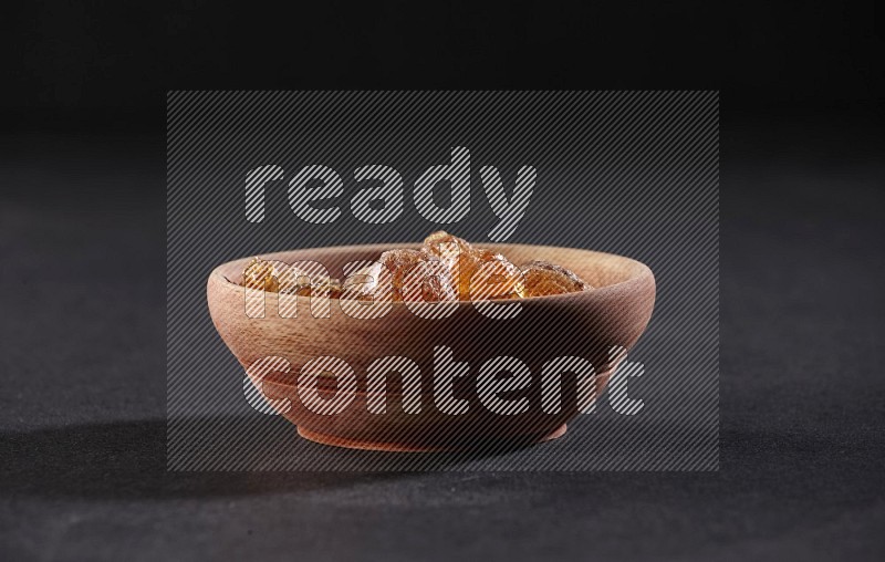 A wooden bowl full of gum arabic on a black flooring in different angles