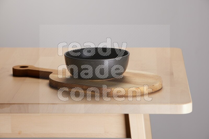 black bowl placed on a  wooden oval cutting board on the edge of wooden table