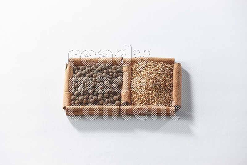 مربعان من أعواد القرفة ممتلئان بحبوب الخردل وحبوب بهار الفلفل الحلو علي خلفية بيضاء