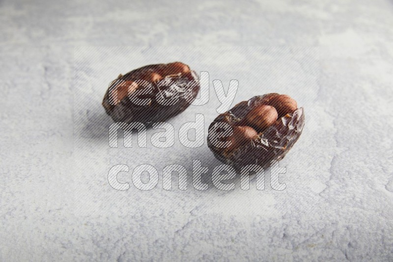 two hazelnuts stuffed madjoul dates on a light grey background