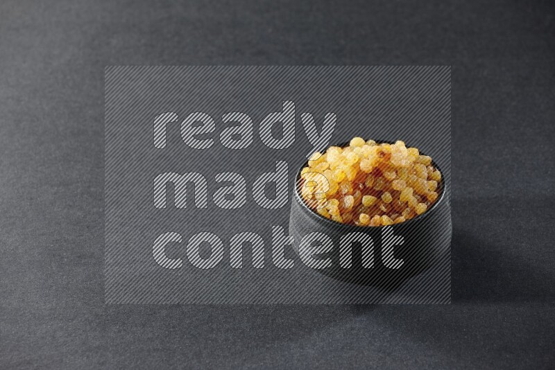 A black pottery bowl full of raisins on a black background in different angles