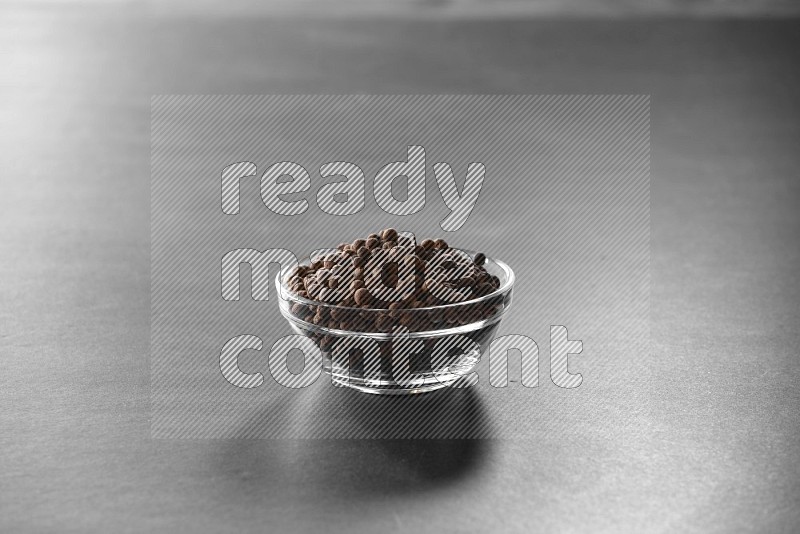 A glass bowl full of allspice on black flooring