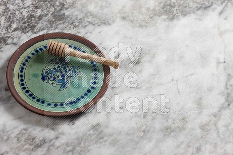 Decorative Pottery Plate with wooden honey handle in it, on grey marble flooring, 65 degree angle