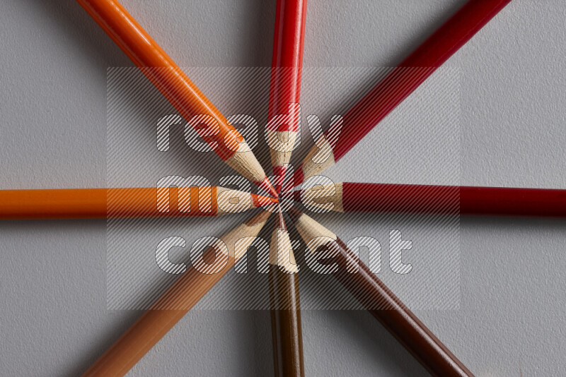 An arrangement of colored pencils in shades of orange and red on grey background