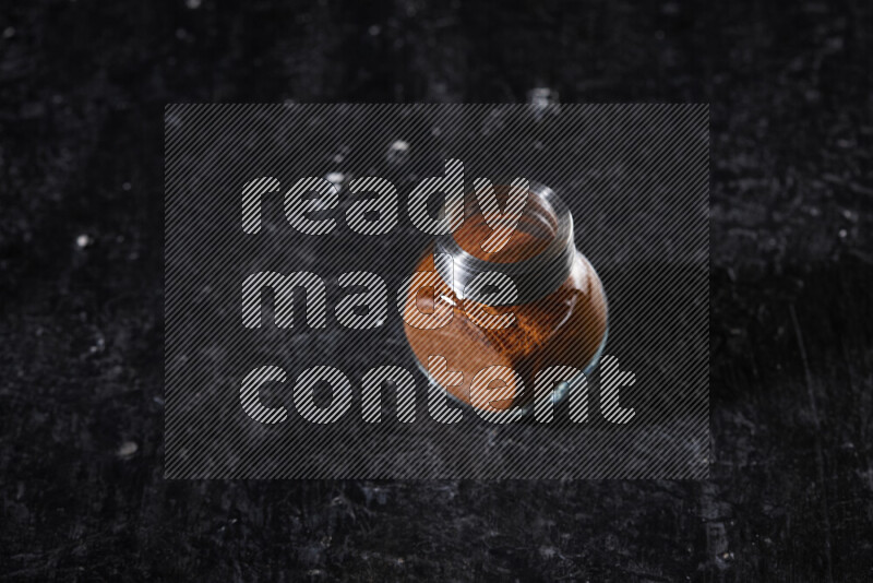 A glass jar full of ground paprika powder on black background